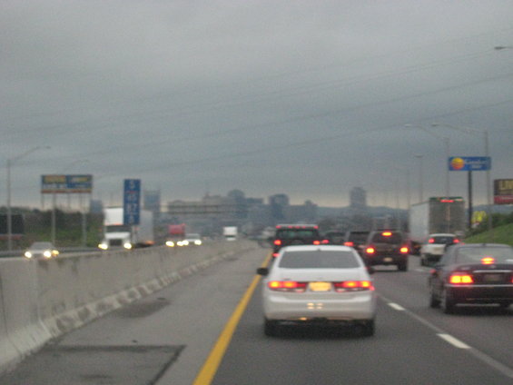 Highway traffic under a cloudy sky with a distant city skyline