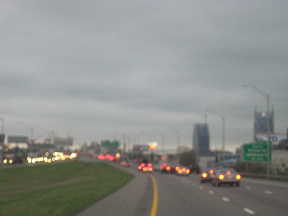 Cars on a highway under a cloudy sky with city buildings in the distance
