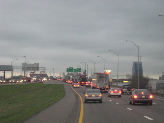 Highway traffic under a cloudy sky with a distant skyscraper