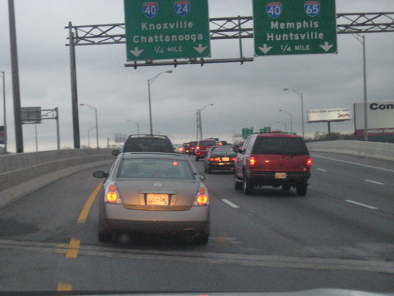 Highway traffic with a tan sedan in the foreground and a red SUV behind it