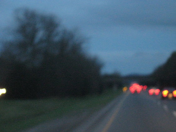 Cars driving on a highway at dusk, with trees on the side