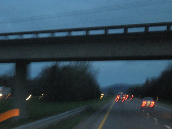 Blurry highway scene at dusk with taillights of cars ahead and an overpass overhead