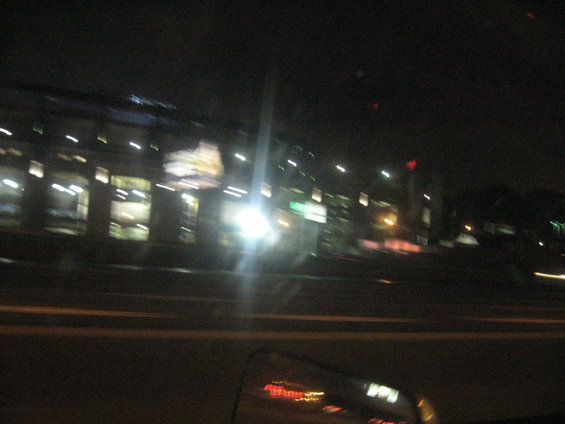 view from car at night, buildings with lights, blurry street