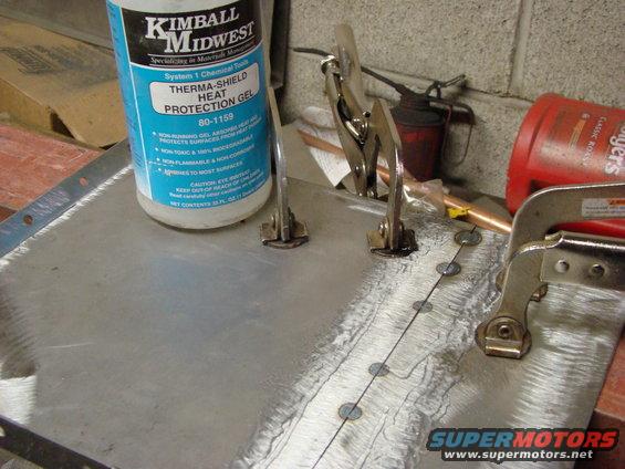Metal sheet clamped for welding, with Kimball Midwest Therma-Shield Heat Protection Gel bottle nearby. A red oil can and a red jug are also visible