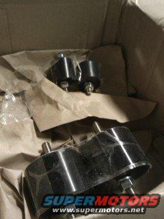 Two black engine mounts in a cardboard box with brown paper packing