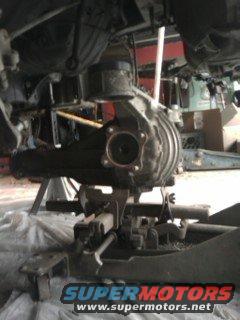 Underside view of a car's differential and suspension components on jack stands. SuperMotors logo visible