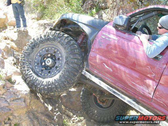 Red Toyota Tacoma off-roading on rocks. Driver is visible inside