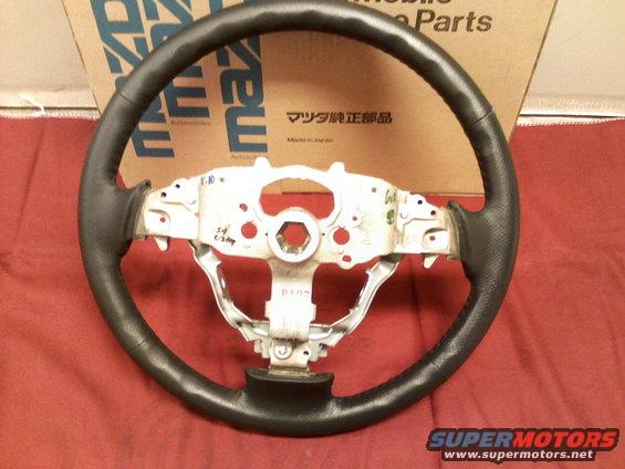 Steering wheel with black leather grip and metal hub, part number visible