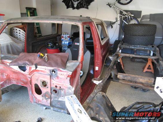 1986 Ford Bronco body shell in a garage, stripped down for restoration. Racing seat visible inside