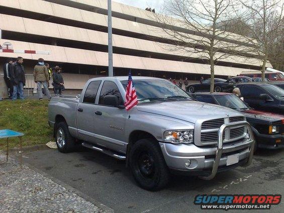 Silver Dodge Ram pickup truck parked in front of a building, with an American flag on the fender