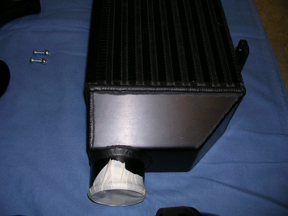 Black intercooler with taped inlet pipe, two bolts nearby on blue cloth