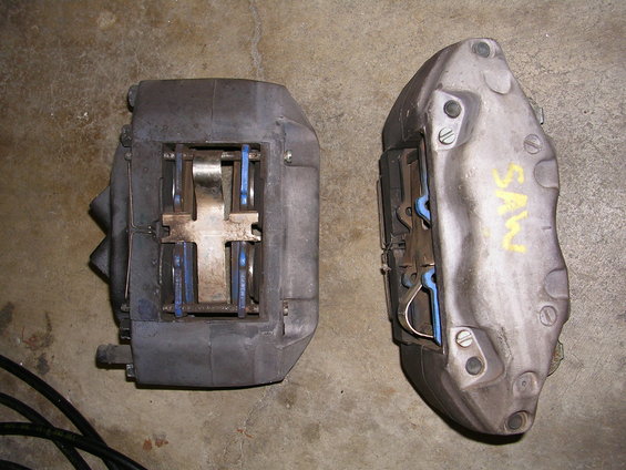 Two brake calipers, one dark gray and one silver with yellow writing that says 'SAW'