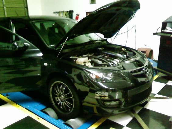 Black car with hood open on a dynamometer, Cobb Tuning sticker on bumper