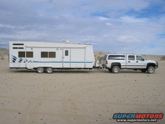 White pickup truck towing a white travel trailer in a sandy, desert landscape