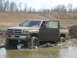 1990 Ford Bronco - A pickup truck is stuck in a muddy off-road area with its door open.