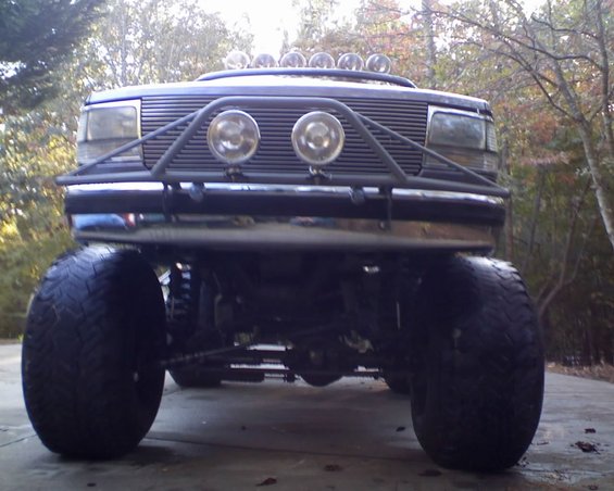 Front view of a lifted 1992 Ford Bronco with large off-road tires, a chrome bumper, and a brush guard with four auxiliary lights