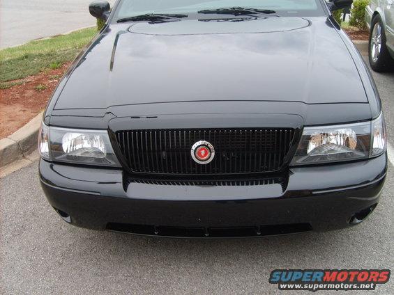 Black sedan front grille with vertical slats and a circular emblem. Headlights are visible