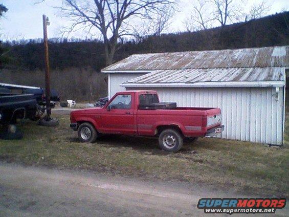 Red 1992 Ford Ranger pickup truck parked next to a white building, side view