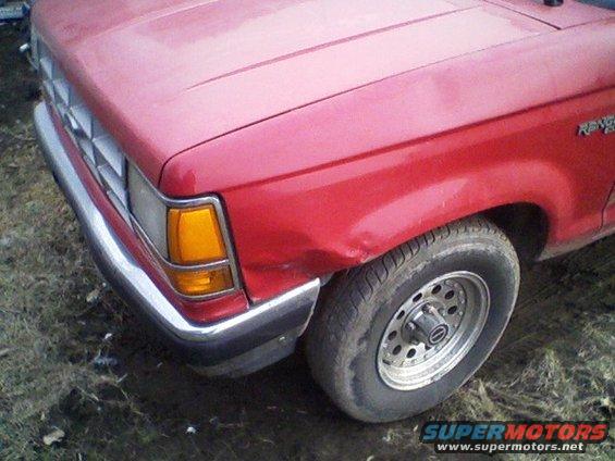 Front fender and headlight of a red pickup truck with a dent near the wheel
