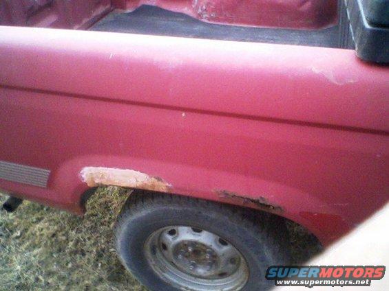 Red pickup truck rear fender with rust and primer visible near the wheel well