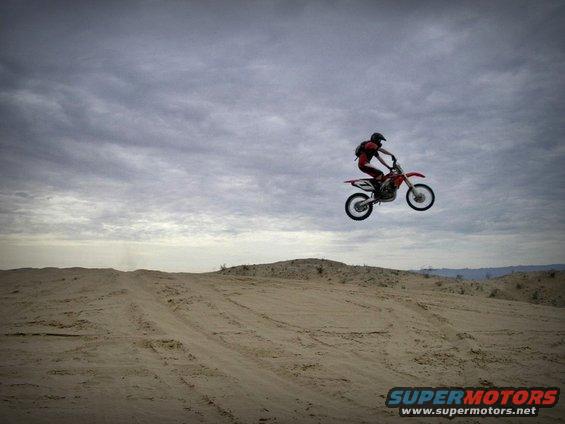 Red dirt bike airborne over sand dunes