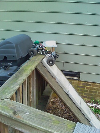 RC rock crawler on a wooden ramp next to a grill