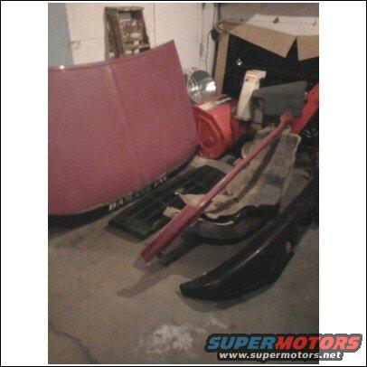 Red hood and black fender parts piled in a garage with boxes and other items