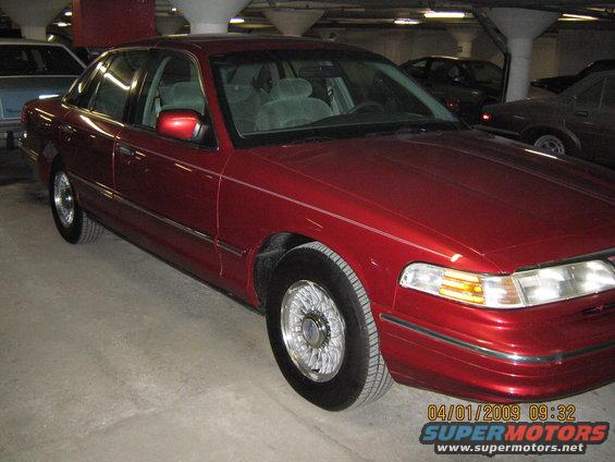 Red 1997 Ford Crown Victoria sedan parked indoors, three-quarter front view. Chrome wheels, light-colored interior visible