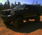 Black 2003 Ford Excursion with aftermarket lift kit and large tires, parked on dirt road