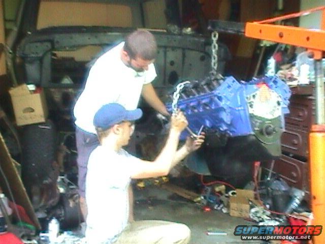 Engine being lowered into a vehicle with two people working on it