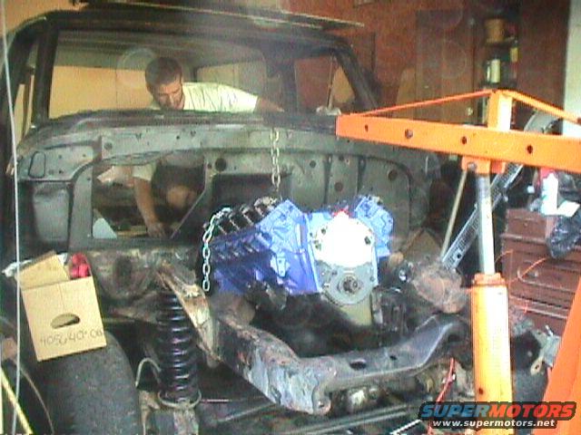1978 Ford Bronco engine bay with engine being lowered by an engine hoist