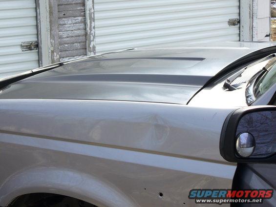 Silver Ford Bronco hood with a dark gray accent and a side mirror. Two small holes are visible on the fender