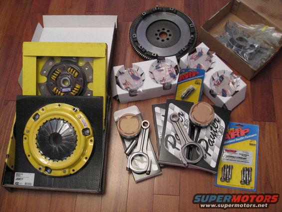 Collection of engine parts: ACT clutch kit, flywheel, Eagle connecting rods, and Wiseco pistons. ARP fasteners also visible