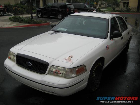 White sedan with black grille, American flag sticker on fender, and a cartoon sticker on the hood