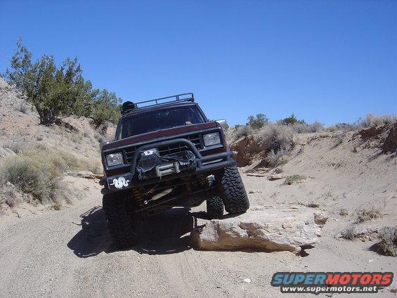 Maroon 1986 Ford Bronco II off-roading on a rocky trail, front bumper with winch, roof rack
