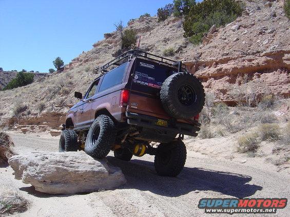 Brown 1986 Ford Bronco II off-roading on a dirt trail, rear view