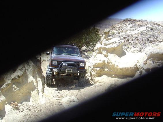 1986 Ford Bronco II driving on a dirt trail between rocky formations