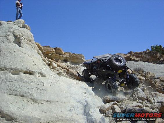 Off-road vehicle climbing rocky terrain with a person standing on a cliff above