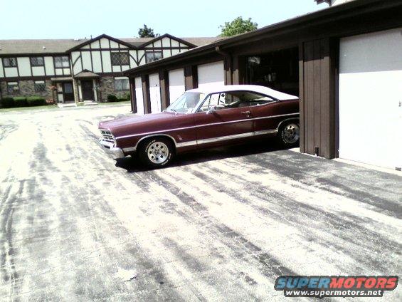 maroon coupe with white roof parked next to garages. It has chrome trim and a white vinyl top