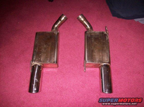 two chrome exhaust mufflers with angled tips, sitting on a red carpet