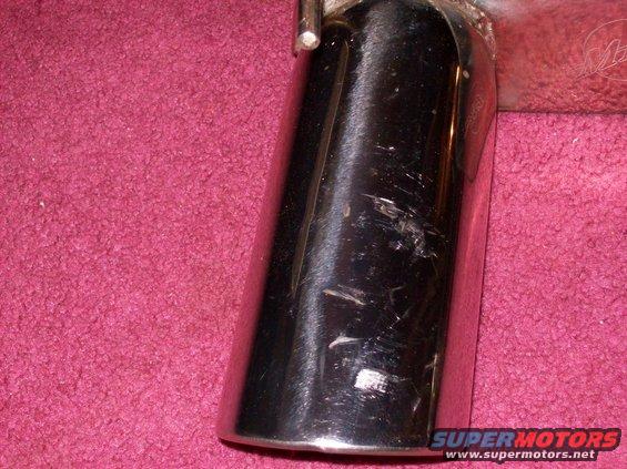 Chrome exhaust tip with scratches on a pink carpeted surface