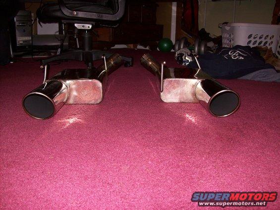 pair of chrome exhaust mufflers with black tips on a pink carpet
