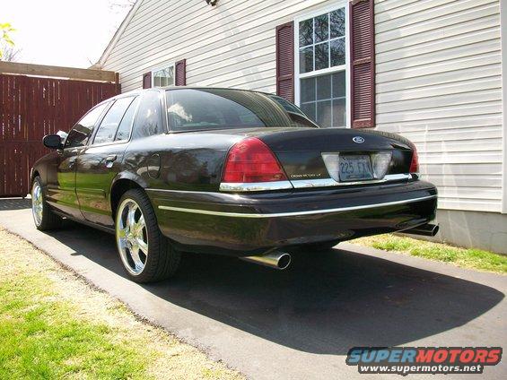 Black 2003 Ford Crown Victoria parked on driveway, rear 3/4 view, chrome wheels, tinted windows