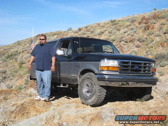 Black and grey Ford Bronco parked on rocky terrain with a man standing beside it