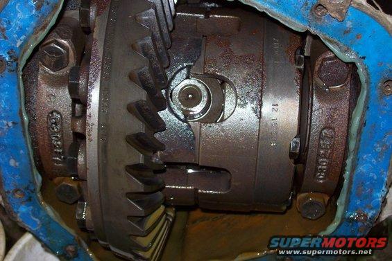 Close-up of differential gears with some blue sealant and oil visible. Part numbers are stamped on the metal