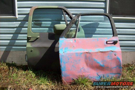 Two truck doors, one in camouflage, the other with faded red and blue paint, leaning against a building