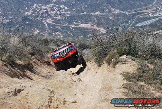 Red off-road truck going down a steep dirt trail with mountains in the background