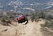 1996 Ford Bronco - A red off-road truck navigates a challenging descent on a dusty mountain trail.