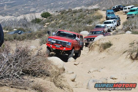 Red Ford Bronco navigating a rocky off-road trail, followed by other SUVs