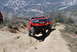 1996 Ford Bronco - A red SUV navigates a steep, rocky trail in a mountainous, arid landscape.